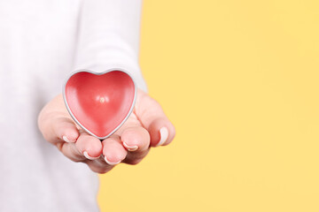 Hand with pink aroma candle, heart shape. Isolated on yellow background.