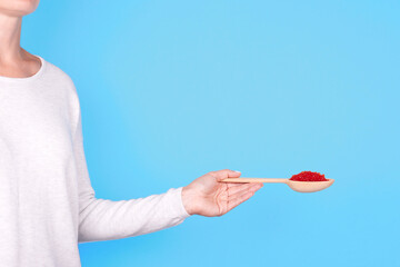 Salmon fish caviar, seafood on wooden spoon in hand, isolated on blue background.