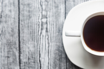 White cup with coffee on a white saucer on a gray wood background