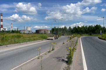 Fototapeta premium Summer landscape with a tractor on the highway shoveling garbage against the background of thermal power plant and yellow flowers