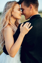 Portrait of young bride and groom enjoying romantic moments outside at sunset in beautiful summer day. Wedding couple. Standing face to face with the green hills on background.