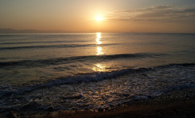 Beautiful dawn over the sea. The sun rises from behind the mountains. Sunny path on the water. Light wave and swell on the surface of the water