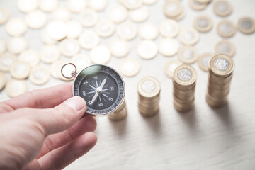 Male hand showing compass. Coins on the white desk