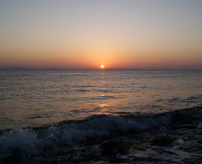 Obraz premium Beautiful dawn over the sea. The sun rises from behind the mountains. Sunny path on the water. Light wave and swell on the surface of the water