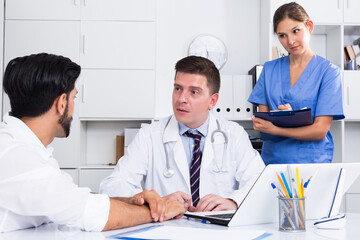 Portrait of confident male doctor listening to patient complaints at clinic
