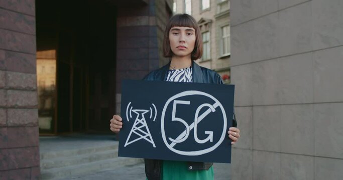 Portrait of millennial woman holding placard with no 5g sign. Young girl with nose ring protesting against new technology and compatible antenna deployment while standing at street