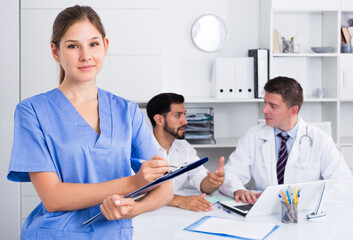 Smiling young female doctor writing notes on clipboard in clinic