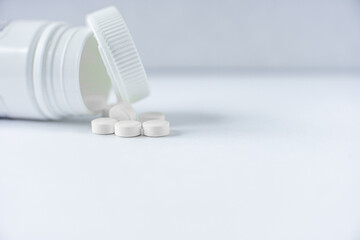 Round small white pills spread out from white plastic bottle a white background with copy space. Pharmaceutical industry. Concept of antibiotic drug resistance, healthcare and pharmaceutics.