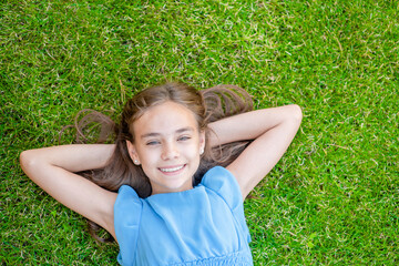 Smiling teen girl lying on a grass, top down view