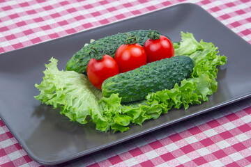 Fresh cucumbers and tomatoes and lettuce on a gray plate. vitamins and light breakfast