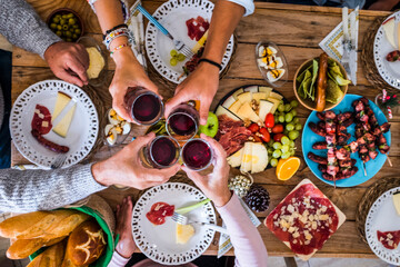 Family and friends clinking and have faun at home during christmas dinner - top view of wooden traditional table with xmas decorations and people celebrating the event