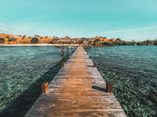 Obraz premium Wooden jetty at sunset, crystal clear water, coral reef and island, Indonesian paradise