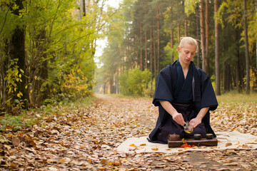 Man in traditional japanese clothes making tea in autumn park