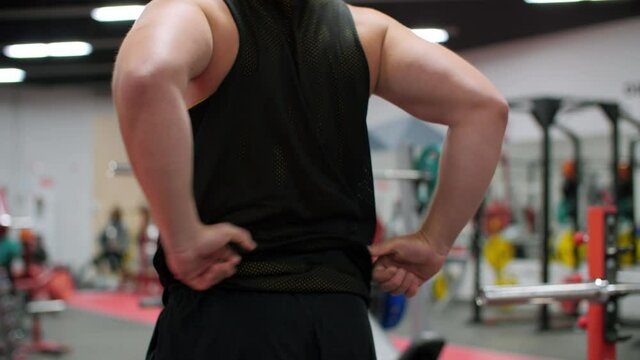 Back view of man stretching muscles before workout in gym. Rear view of muscular man in sportswear exercising in gym