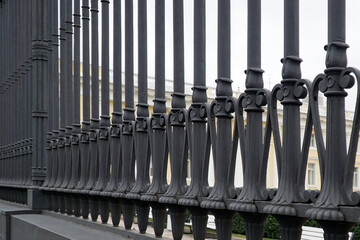 Fragment of forged decorative iron fence. A row of round bars of a cast-iron fence with wrought iron ornaments.