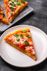 Hot pizza slices with mozzarella cheese, ham, tomato and parsley on wooden cutting board and plate, stone concrete background, angle view macro