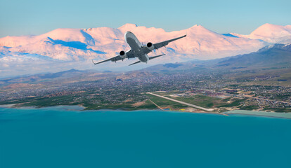 Fototapeta na wymiar Airplane taking off from airport - Passenger airplane is flying over amazing snowy mountains and sea - Travel by air transport