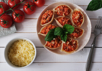 Italian pasta Conchiglioni  stuffed with bolognese sauce and sprinkled with cheese on white wooden table. Served with basil. Top view. Close-up.