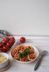 Italian pasta Conchiglioni  stuffed with bolognese sauce and sprinkled with cheese on white wooden table. Served with basil. Selective focus, side view. Copy space.