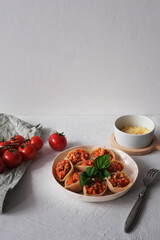 Italian pasta Conchiglioni  stuffed with bolognese sauce and sprinkled with cheese on white concrete surface. Served with basil. Side view. Copy space.