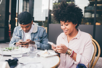 Fototapeta na wymiar Couple sitting restaurant using mobile phone - Diverse black man and woman ignoring using smartphone at restaurant - phubbing, overuse, addiction concept
