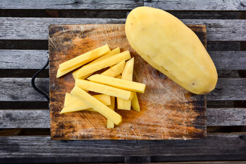 Potatoes sliced sticks for french fries on chopping board and wood table background. Fresh potato pieces cut bar on cutting board with peel