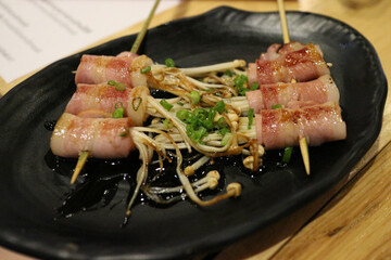 Grilled bacon with enoki mushroom on black plate