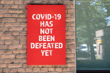 COVID-19 HAS NOT BEEN DEFEATED YET. Red advertising sign on the masonry wall