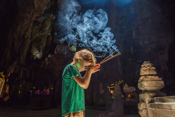 Young boy praying in a Buddhist temple holding incense Huyen Khong Cave with shrines, Marble...