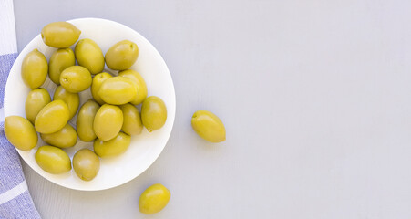 Banner with olives on a white plate. Still life with a towel on a gray table, space for text.