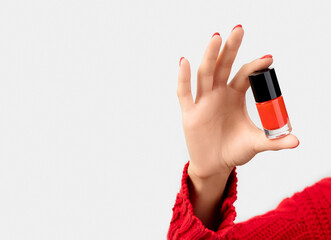 Woman's hand in sweater with red manicure holding a bottle of nail polish