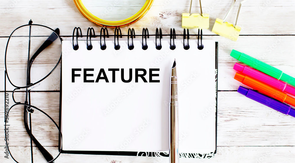 Aufkleber feature written in a notebook on white background with office tools