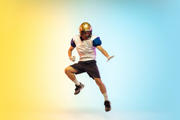 Fototapeta na wymiar Unstoppable. American football player isolated on gradient studio background in neon light. Professional sportsman during game playing in action and motion. Concept of sport, movement, achievements.