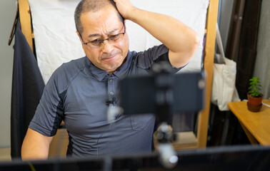 スマートフォンをウェブカメラにしてオンラインミーティングしている男性が頭を抱えしかめっ面をして困っている様子