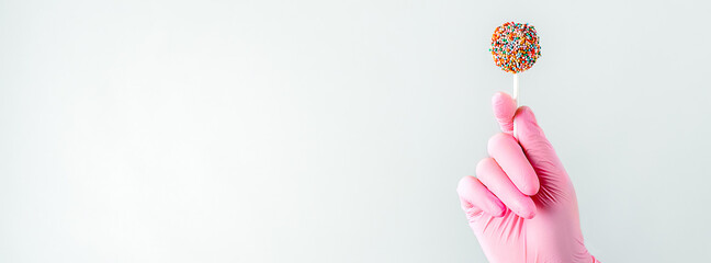 Closeup of human hand in pink surgical gloves holding and showing colorful candy in hand. Isolated over white background. Copy space for your text