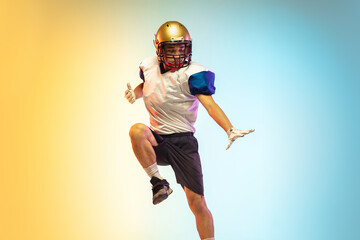 Fototapeta na wymiar Inspired. American football player isolated on gradient studio background in neon light. Professional sportsman during game playing in action and motion. Concept of sport, movement, achievements.