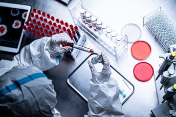 血液サンプルとワクチンを手にする防護服を着た研究員	