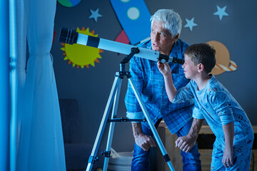 Child with grandfather using telescope during night