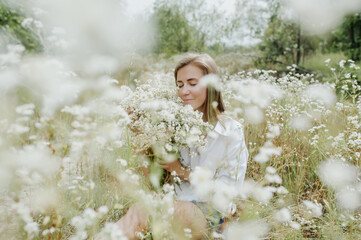 Beautiful woman with closed eyes enjoys smelling wild flowers while sitting in the nature.