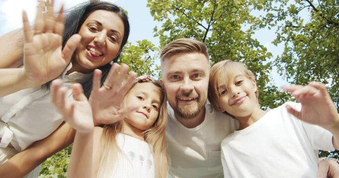 Happy family taking selfie or recording video leaning over the camera smiling and waving during summer vacation. Weekend and travel concept.