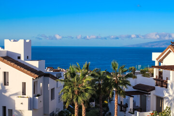 White houses among palm trees overlooking the Atlantic Ocean and La Gomera island against the blue sky