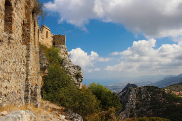 Fototapeta na wymiar Stone towers of the castle of Saint Hilarion against a blue sky with clouds. The mountains of Cyprus and the view down to Kyrenia and the Mediterranean sea. Cyprus.