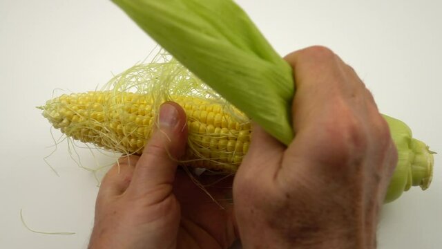 Man peels an ear of corn before cooking on the white table, slow motion