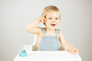 Blond baby with striped overalls sitting and gesturing