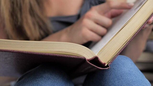 A woman' s hand holds a book and moves his fingers along the page while reading. The reader of the book holds 4k