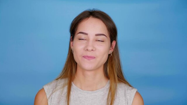 Beautiful funny woman in gray t-shirt talking, squinting and smiling on blue background with copy space. 4K slow motion footage