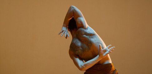 Young guy dancer without shirt in neon golden light. Dance school poster. Body with tattoos. View from back