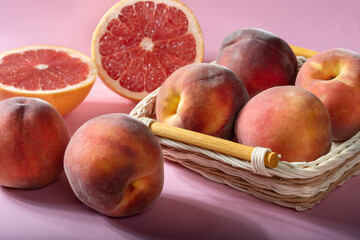 Ripe grapefruit with juicy peaches on a pink background in a basket.