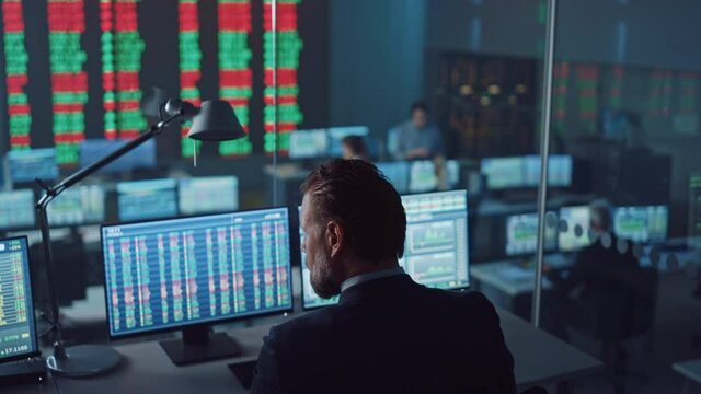 Professional Financial Data Analysts Working in a Modern Monitoring Office with Live Analytics Feed on a Big Digital Screen. Monitoring Room with Finance Specialists Sit in Front of Computers. 