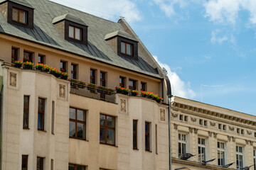 An old tenement house on the square. Beautiful blue sky in the background. Red flowers on the balcony.